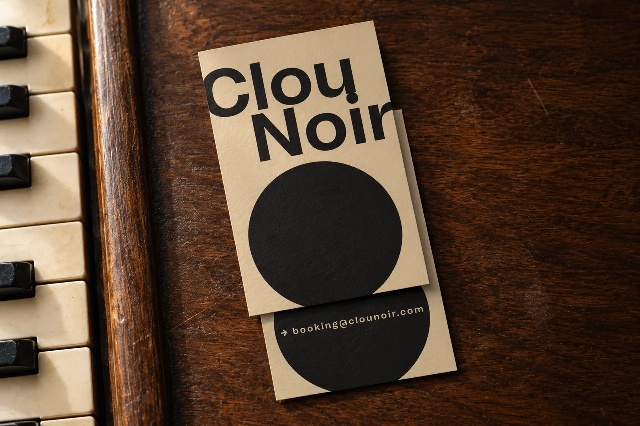 KI-Mockup des Corporate Designs für Clou Noir: überlappende beige Visitenkarten auf dunklem Klavierholz, daneben ein Ausschnitt der Tasten.