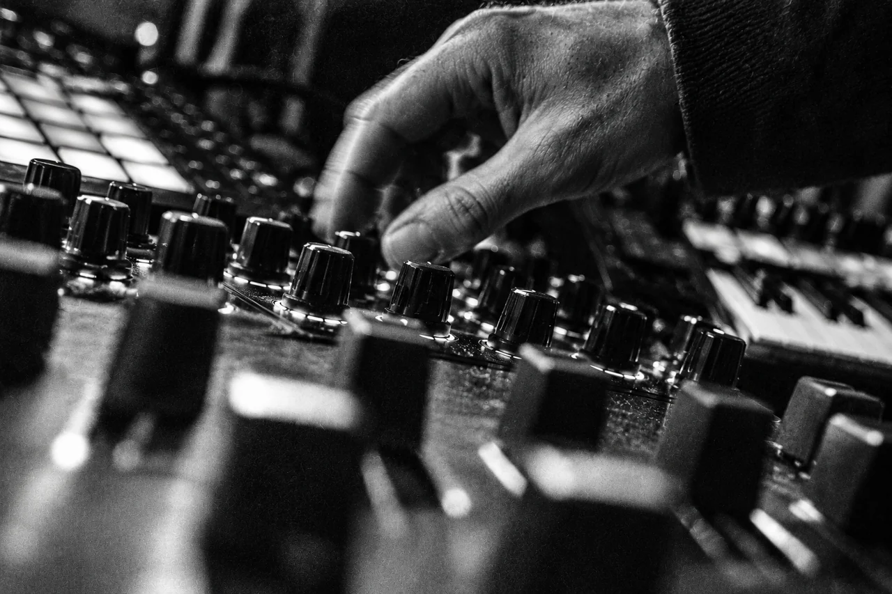 Generierte, körnige Schwarz-Weiß-Nahaufnahme einer Hand an Reglern und Fadern eines Musik-Setups.