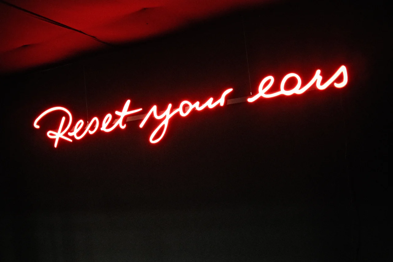 Leuchtender Schriftzug Reset your ears in einem dunklen Raum.